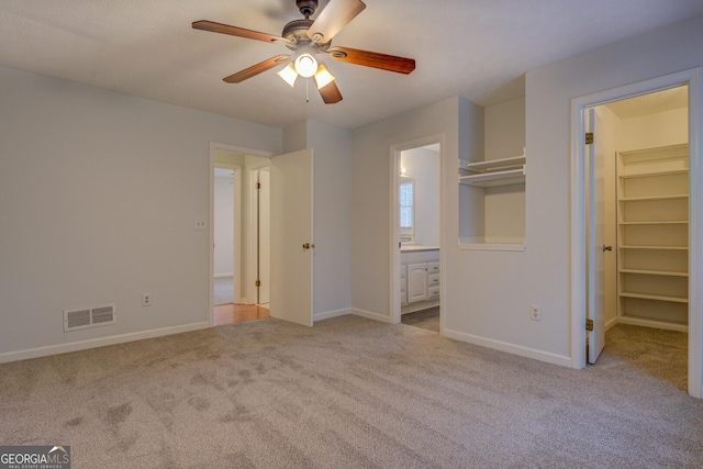 unfurnished bedroom with light carpet, a walk in closet, ensuite bath, ceiling fan, and a closet