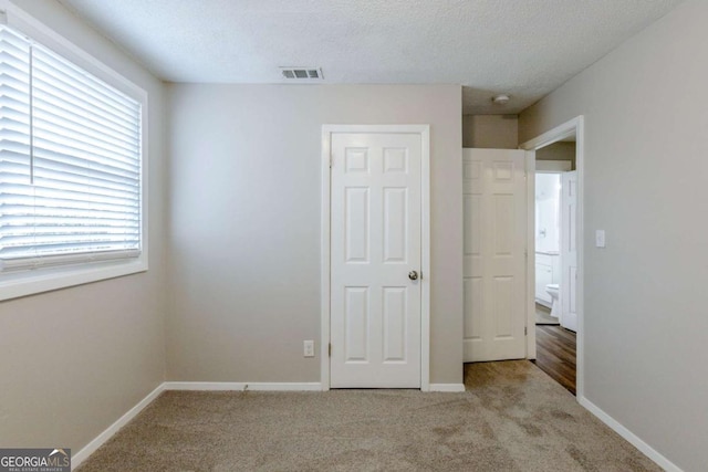 unfurnished bedroom with multiple windows, light colored carpet, and a textured ceiling