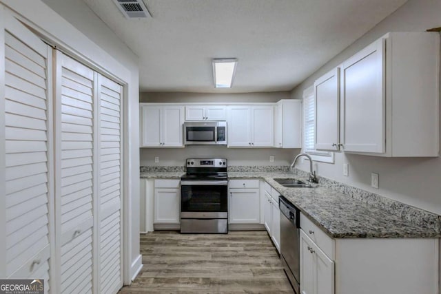 kitchen with light stone counters, sink, white cabinetry, and stainless steel appliances