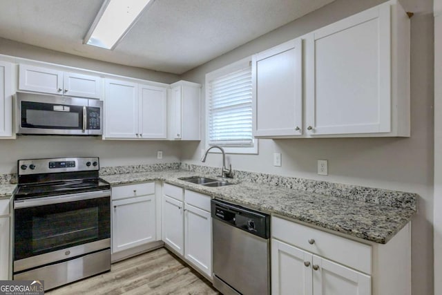 kitchen featuring light stone countertops, sink, stainless steel appliances, light hardwood / wood-style floors, and white cabinets