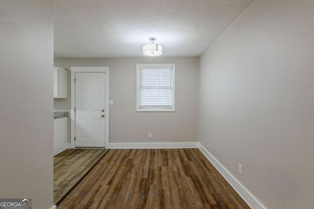 unfurnished dining area with a textured ceiling and dark wood-type flooring