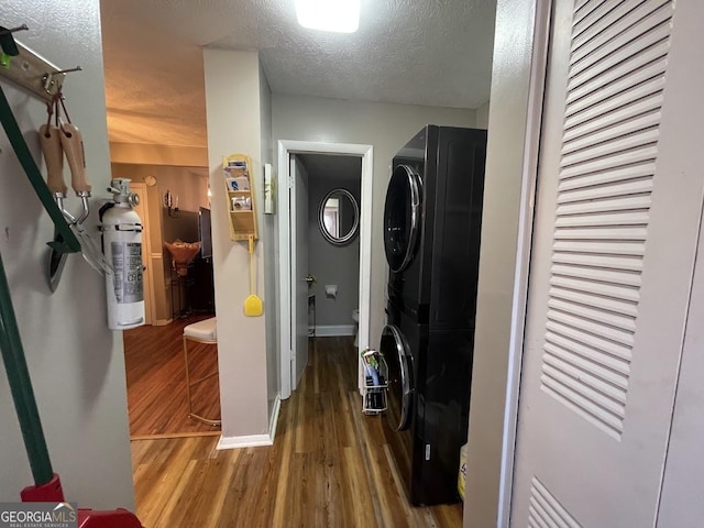 clothes washing area featuring stacked washing maching and dryer, wood-type flooring, and a textured ceiling