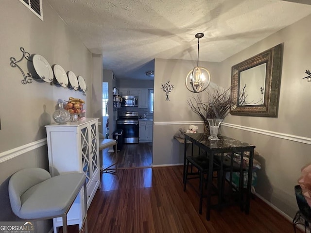 dining space featuring a textured ceiling, a notable chandelier, and dark hardwood / wood-style flooring