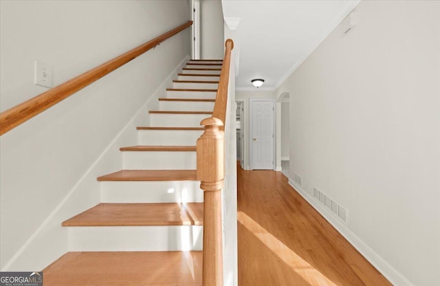 stairway with wood-type flooring and crown molding