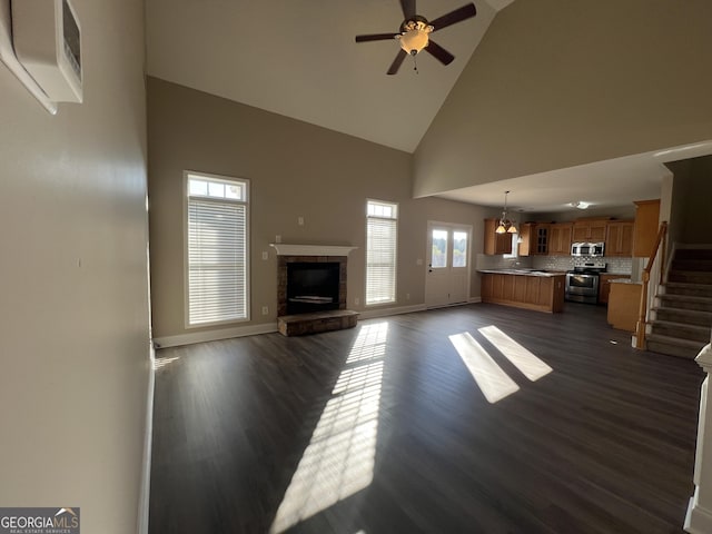 unfurnished living room featuring a fireplace, high vaulted ceiling, dark hardwood / wood-style floors, and ceiling fan with notable chandelier