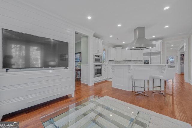 kitchen with a breakfast bar, white cabinetry, island exhaust hood, and built in refrigerator