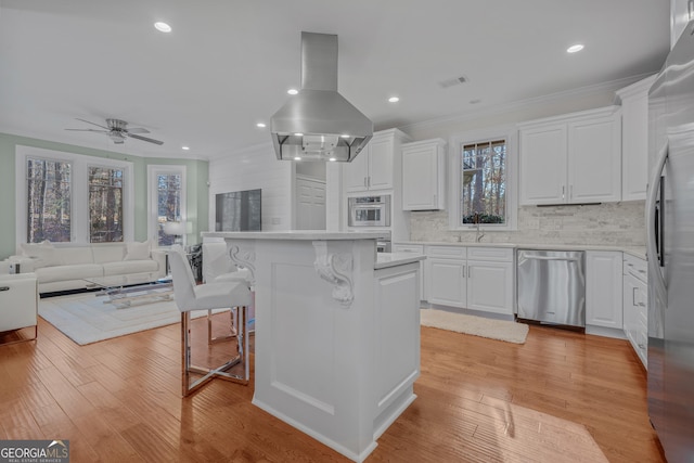 kitchen featuring white cabinets, a kitchen breakfast bar, island exhaust hood, and appliances with stainless steel finishes