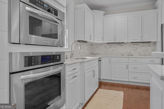 kitchen with sink, white cabinetry, crown molding, and stainless steel oven