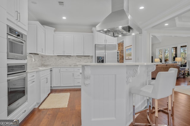 kitchen with island exhaust hood, backsplash, stainless steel appliances, sink, and white cabinetry