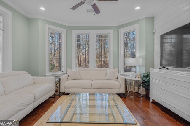 living room with a wealth of natural light, ceiling fan, dark wood-type flooring, and ornamental molding