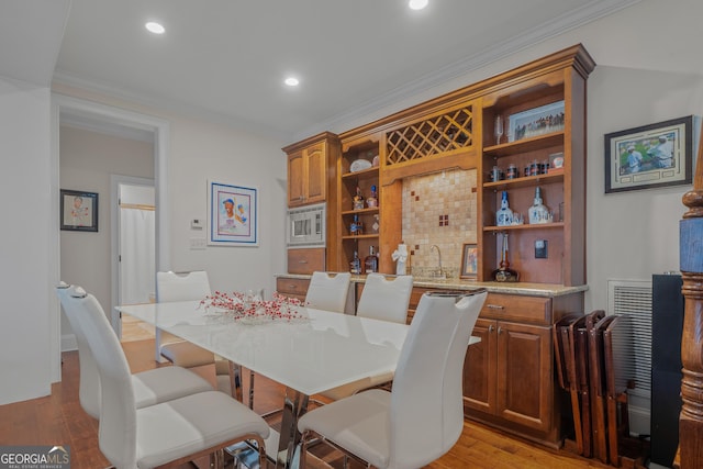 dining space featuring bar area, light hardwood / wood-style floors, and crown molding