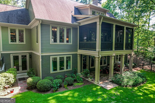 back of property with french doors, a sunroom, and a lawn