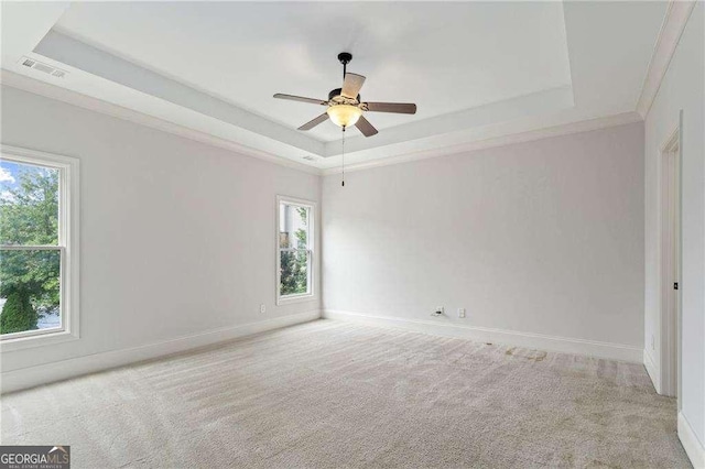 unfurnished room with light colored carpet, ceiling fan, a raised ceiling, and ornamental molding