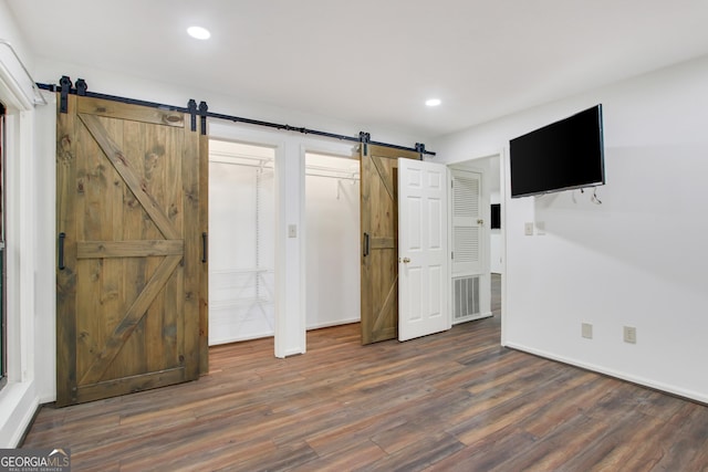 unfurnished bedroom featuring a barn door and dark wood-type flooring