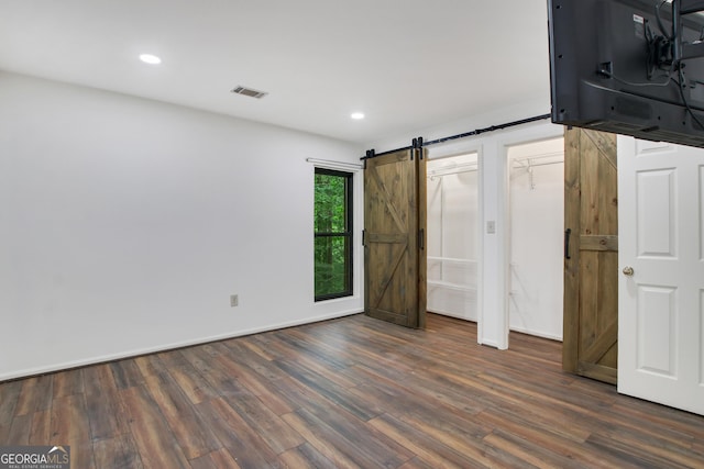 unfurnished bedroom featuring dark hardwood / wood-style floors and a barn door