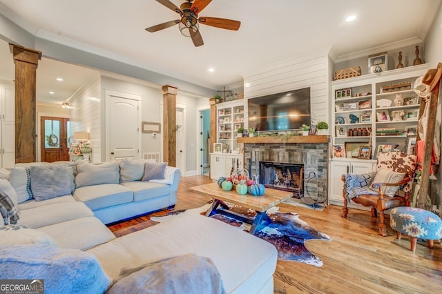 living room with a stone fireplace, ceiling fan, ornamental molding, and light wood-type flooring