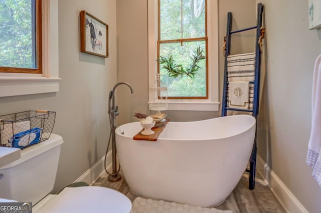 bathroom featuring a tub to relax in, plenty of natural light, and toilet