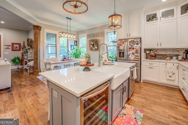 kitchen featuring white cabinets, pendant lighting, an island with sink, and beverage cooler