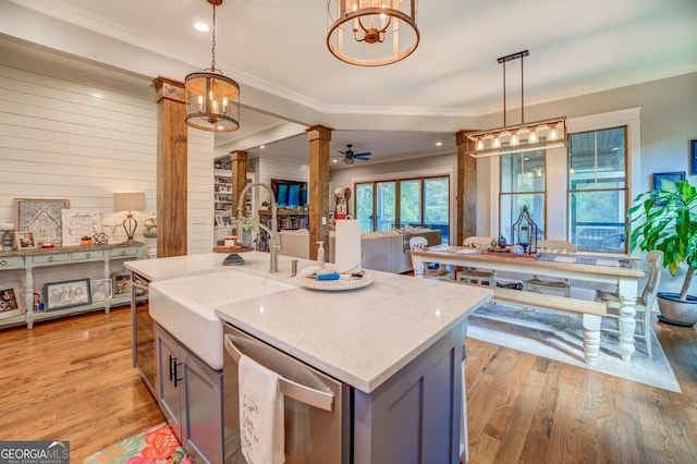 kitchen with decorative columns, stainless steel dishwasher, hanging light fixtures, and a center island with sink