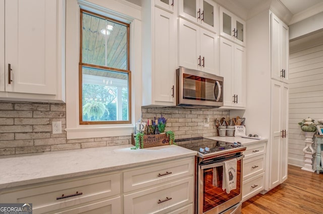 kitchen featuring light stone countertops, appliances with stainless steel finishes, light wood-type flooring, decorative backsplash, and white cabinetry