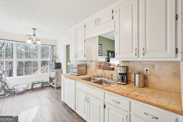 kitchen with pendant lighting, backsplash, white dishwasher, sink, and white cabinetry