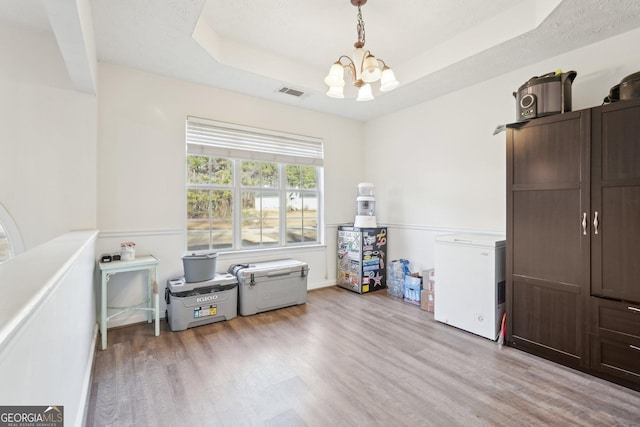 miscellaneous room with a raised ceiling, light hardwood / wood-style flooring, and a chandelier