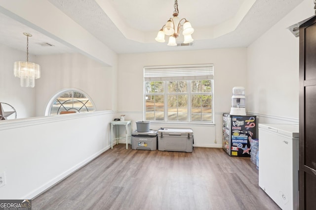 dining area with a raised ceiling, a healthy amount of sunlight, light wood-type flooring, and an inviting chandelier