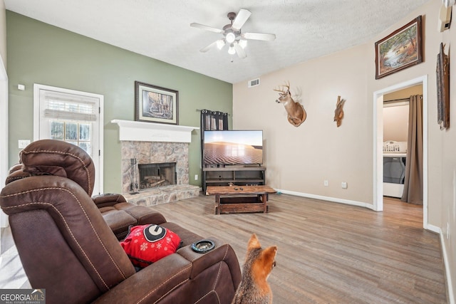 living room featuring ceiling fan, a fireplace, a textured ceiling, and light wood-type flooring