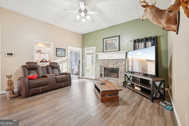 living room featuring a fireplace, ceiling fan, light hardwood / wood-style floors, and a textured ceiling