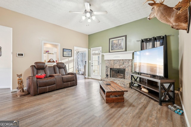 living room featuring a stone fireplace, ceiling fan, wood-type flooring, and a textured ceiling