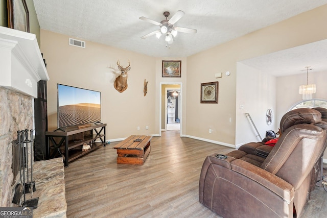 living room featuring hardwood / wood-style floors, ceiling fan with notable chandelier, and a textured ceiling