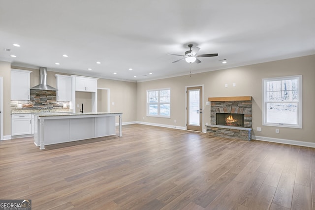 unfurnished living room featuring a fireplace, sink, ornamental molding, ceiling fan, and light hardwood / wood-style floors