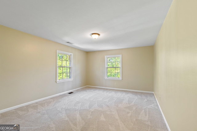 carpeted empty room featuring baseboards, visible vents, and a wealth of natural light