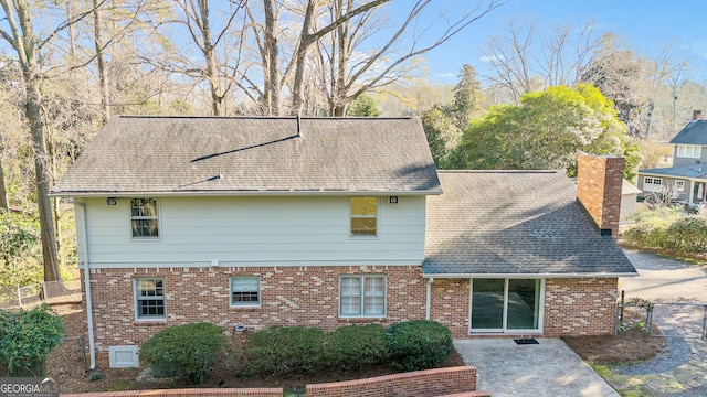 exterior space with brick siding, fence, a chimney, and roof with shingles