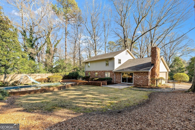 rear view of property featuring a fenced in pool, a chimney, fence, a yard, and brick siding