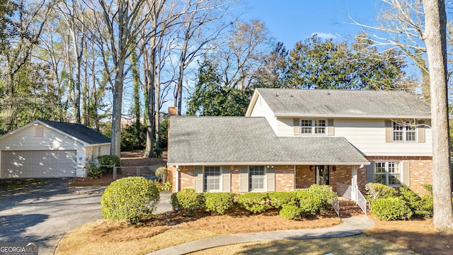 traditional-style home featuring a shingled roof, a chimney, a detached garage, an outbuilding, and brick siding