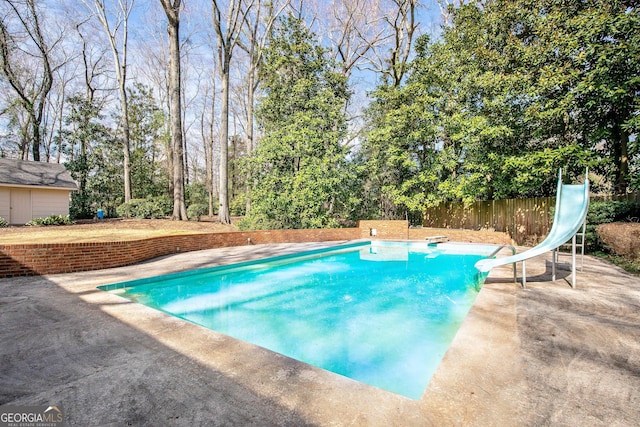 pool with a water slide, a patio area, and fence