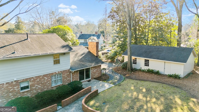 view of front of house featuring brick siding, a patio, a chimney, roof with shingles, and an outdoor structure