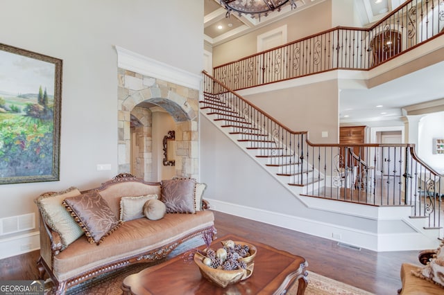 living room featuring hardwood / wood-style floors, a towering ceiling, crown molding, and decorative columns