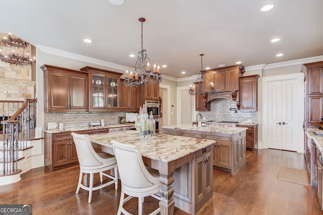 kitchen with light stone countertops, dark wood-type flooring, tasteful backsplash, an island with sink, and pendant lighting