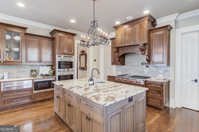 kitchen with sink, an island with sink, appliances with stainless steel finishes, tasteful backsplash, and light stone counters