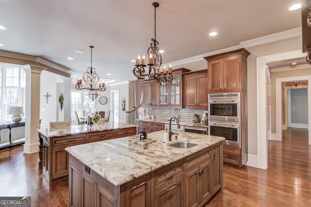 kitchen with pendant lighting, a kitchen island with sink, sink, and crown molding