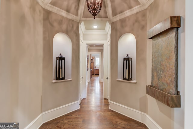 corridor featuring a towering ceiling, coffered ceiling, ornamental molding, hardwood / wood-style flooring, and a notable chandelier