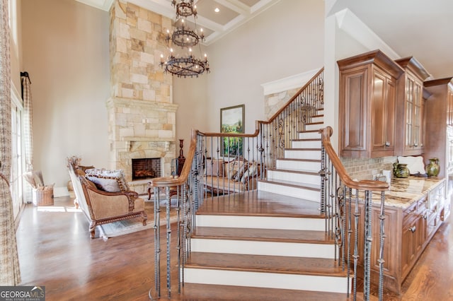 stairway with beam ceiling, a high ceiling, coffered ceiling, an inviting chandelier, and a fireplace