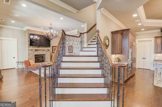 staircase with hardwood / wood-style flooring, a fireplace, a chandelier, and ornamental molding