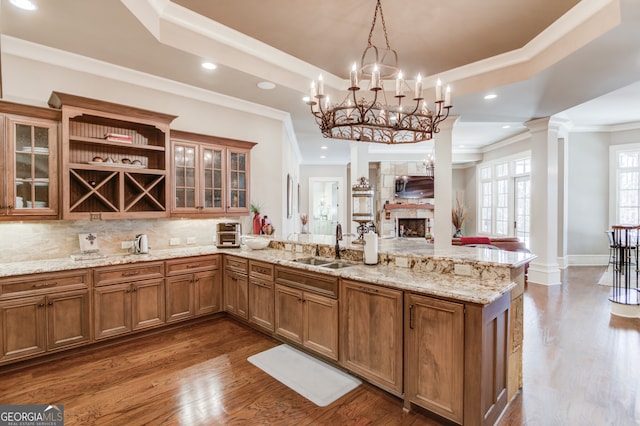 kitchen featuring decorative columns, ornamental molding, sink, decorative light fixtures, and a stone fireplace