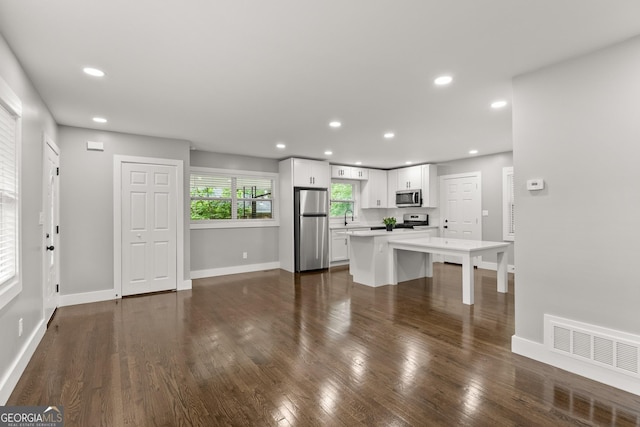 kitchen with sink, dark wood-type flooring, appliances with stainless steel finishes, white cabinetry, and a kitchen island