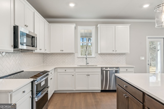 kitchen with white cabinets, appliances with stainless steel finishes, light countertops, crown molding, and a sink