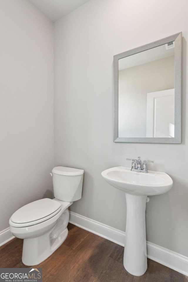 half bath with a sink, wood finished floors, toilet, and baseboards