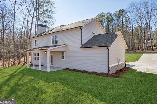 back of property with a shingled roof, a lawn, a chimney, and a patio